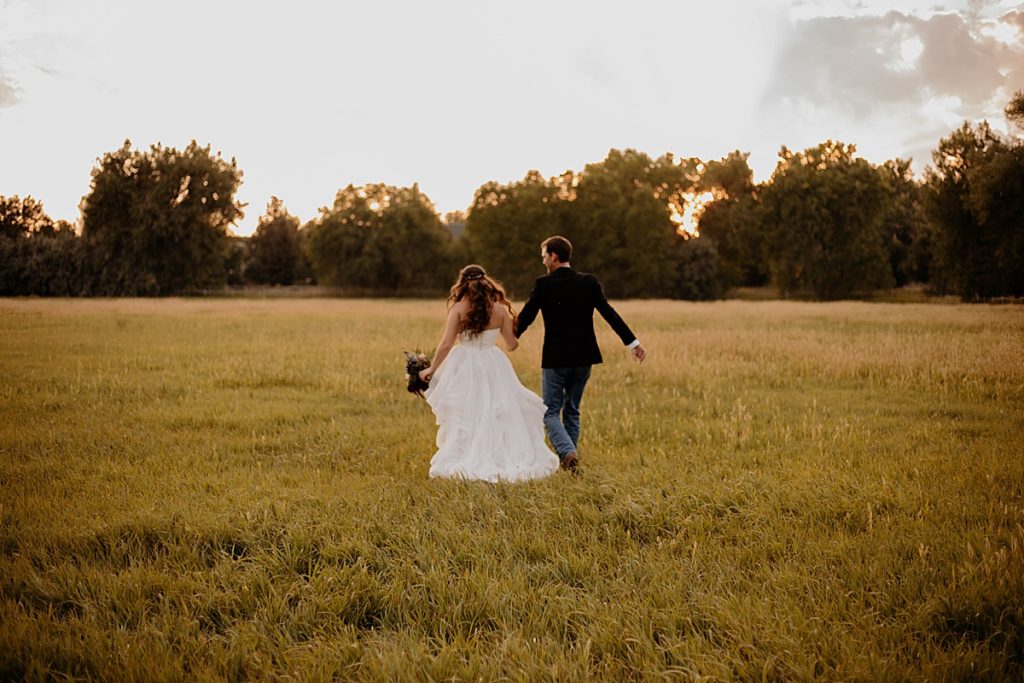 bride and groom running away on field holding hands