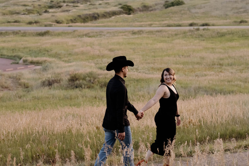 couple holding hands walking in field in colorado